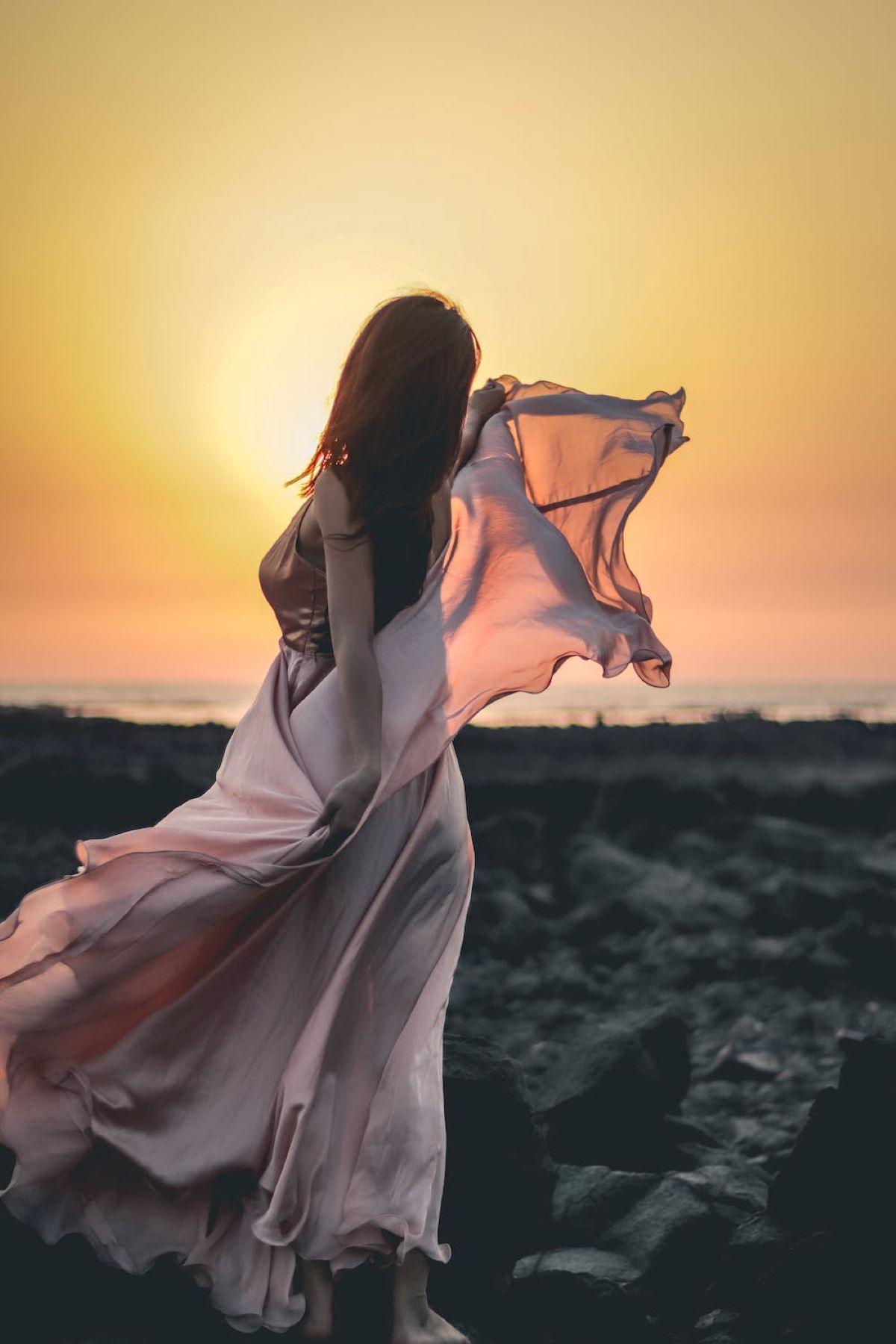 Sensual woman in silk dress on coast at sunset

